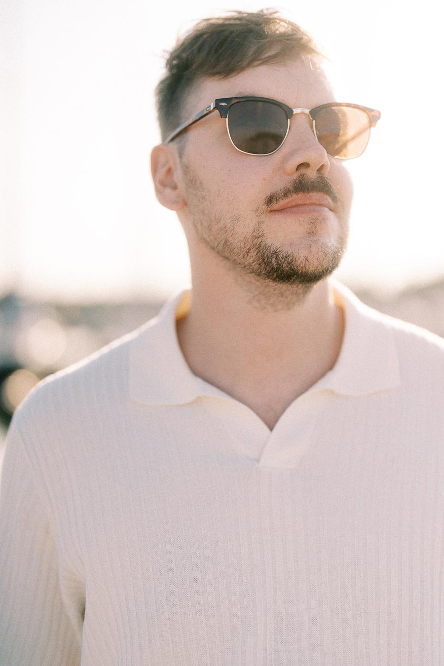 Devin wearing sunglasses and a white knit polo in soft golden hour light at the marina.