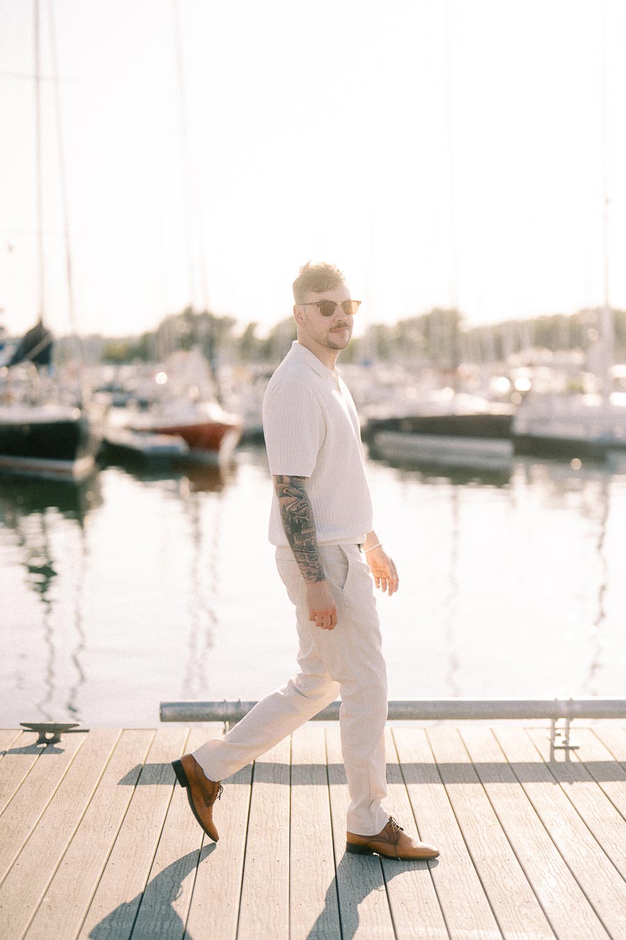 Devin walking on a marina dock in sunglasses during a golden hour engagement session in Hamilton.
