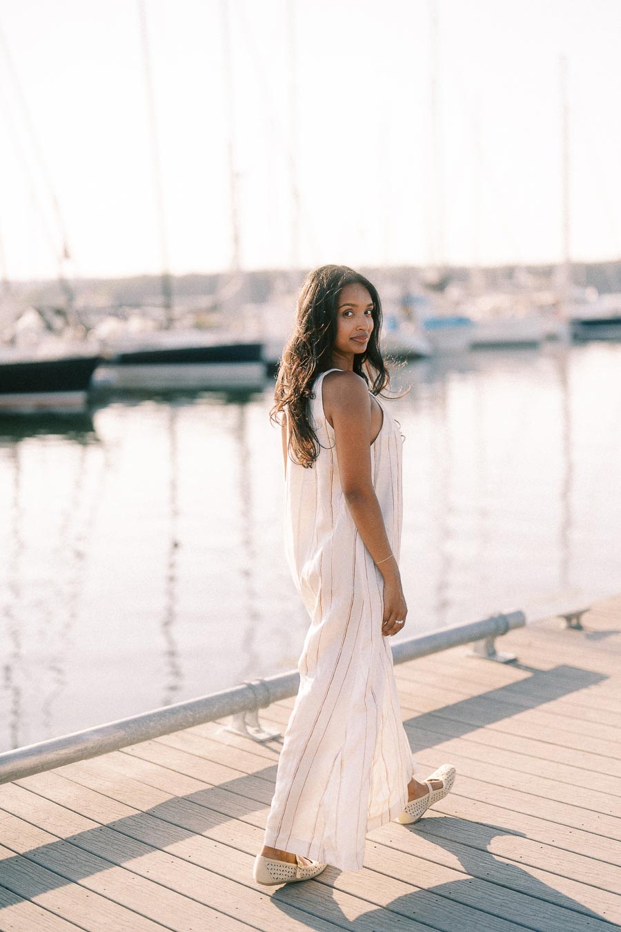 Amber walking on a marina dock beside sailboats during a golden hour engagement session.