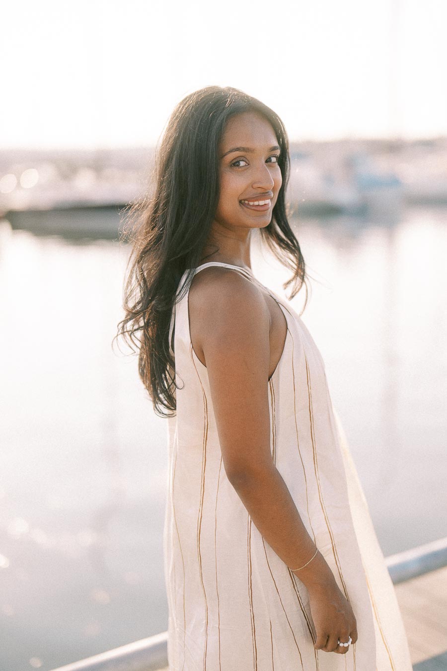 Amber smiles over her shoulder on a marina dock during a golden hour engagement session.