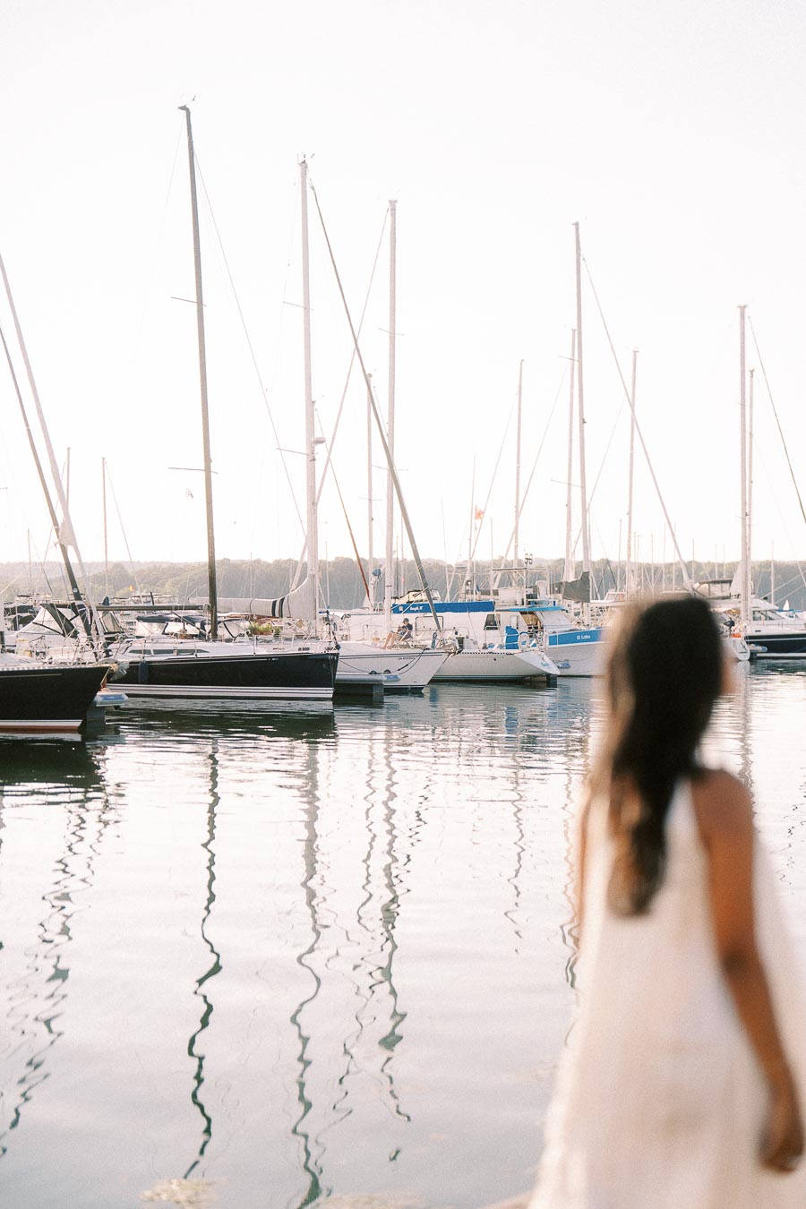 Blurred woman looking toward sailboats reflected in the marina at golden hour in Hamilton, Ontario.