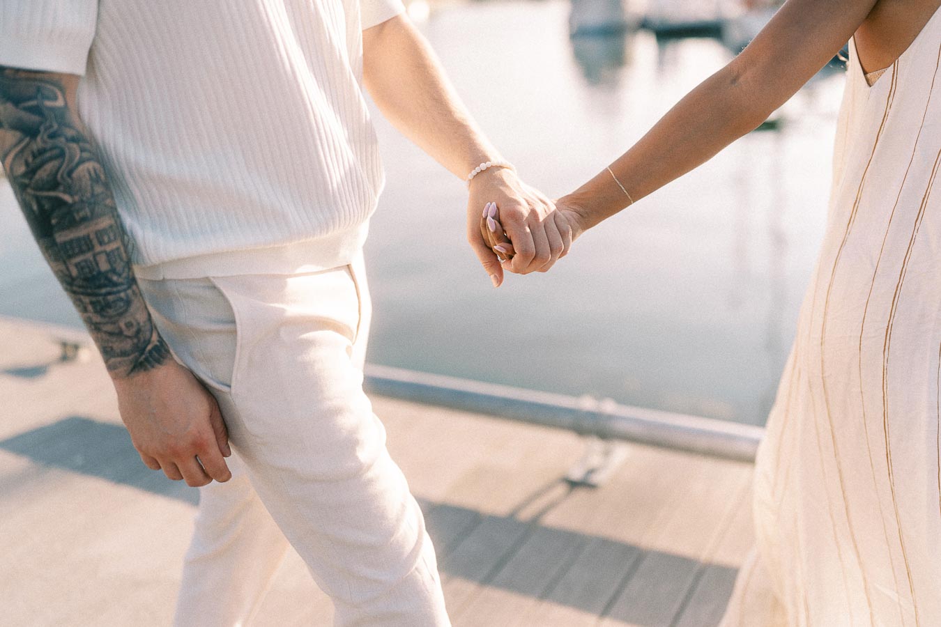 Couple holding hands while walking along a marina dock at golden hour in Hamilton, Ontario.