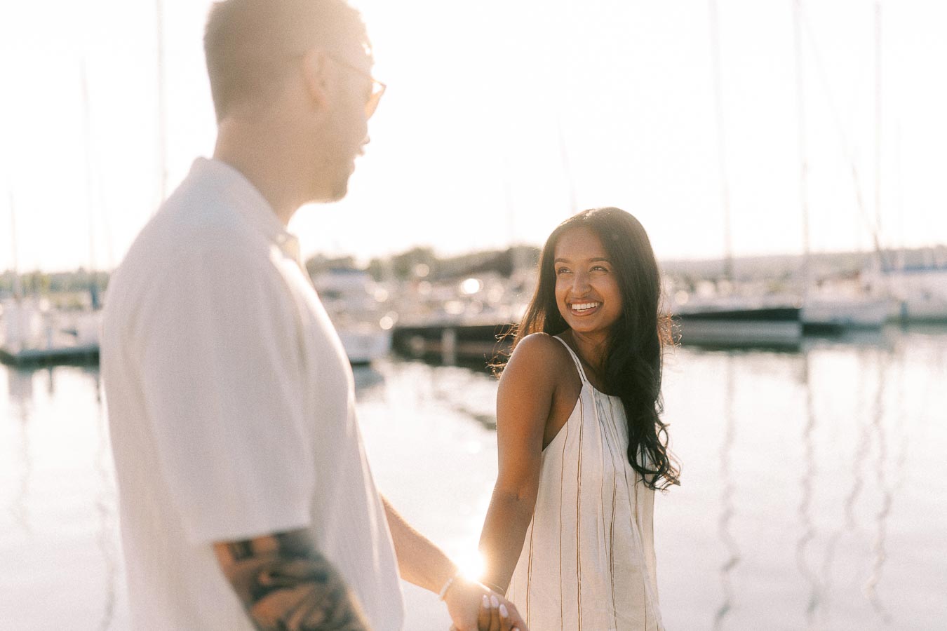 Amber and Devin holding hands at a marina during a golden hour engagement session.