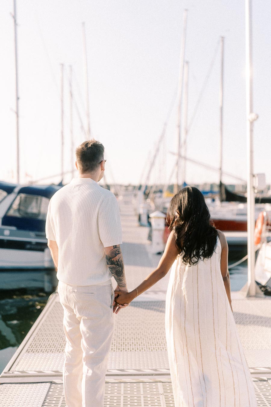 Amber and Devin walk hand in hand along a marina dock at Royal Hamilton Yacht Club.