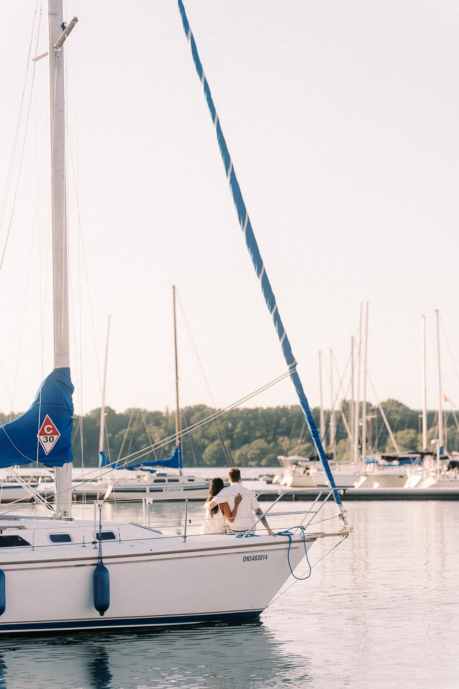 Amber and Devin sit together on a sailboat in a Hamilton marina at golden hour.