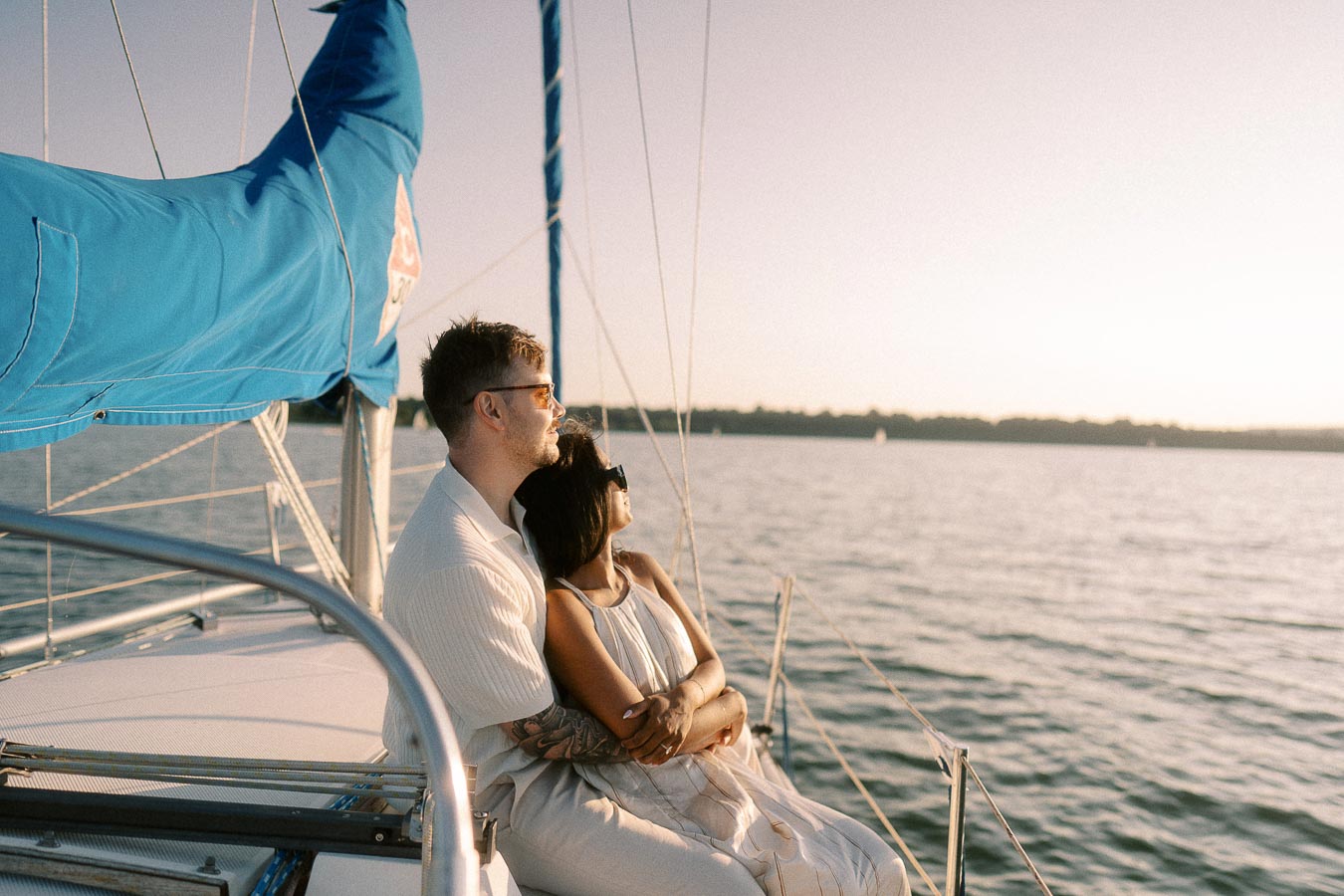 Amber and Devin sit embraced on a sailboat at sunset on Lake Ontario.