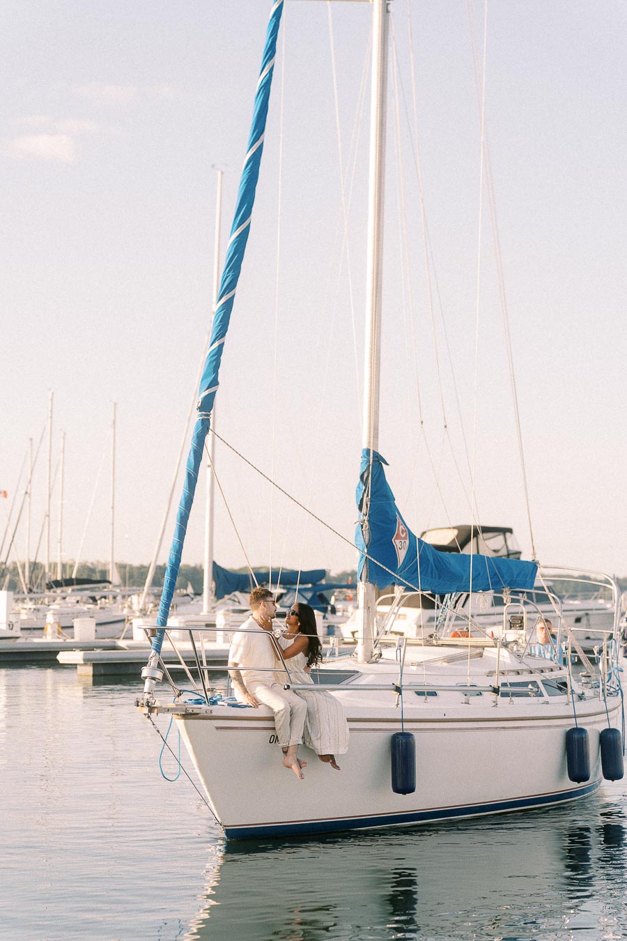 Amber and Devin sit together on a sailboat in a marina at golden hour in Hamilton, Ontario.