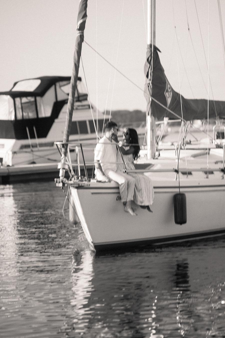 Amber and Devin sitting together on a sailboat in a marina during their engagement session.
