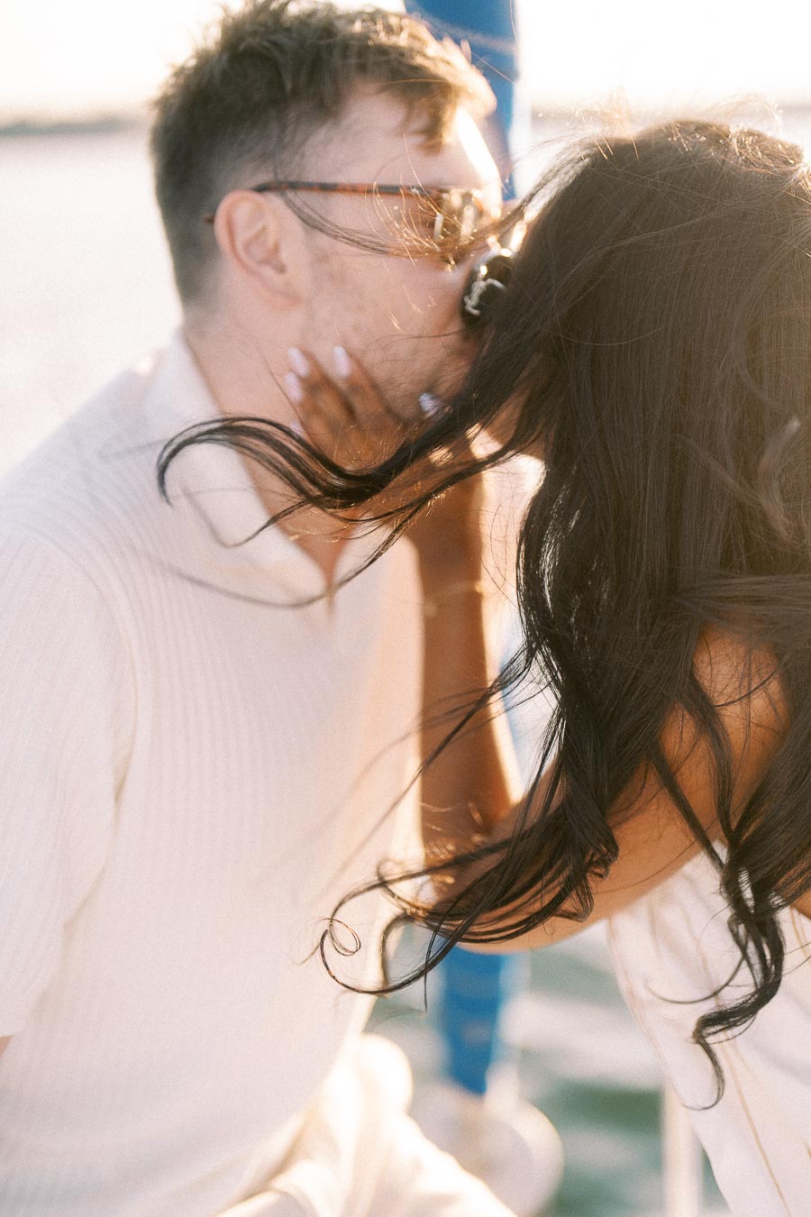 Amber and Devin kiss in warm sunlight during their sailboat engagement session on Lake Ontario.