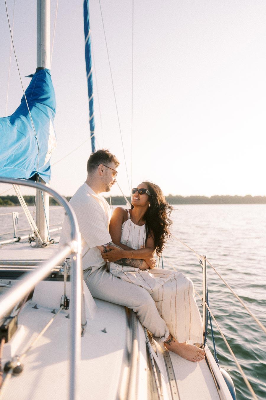 Amber and Devin sitting together on a sailboat during a golden hour engagement session on Lake Ontario.