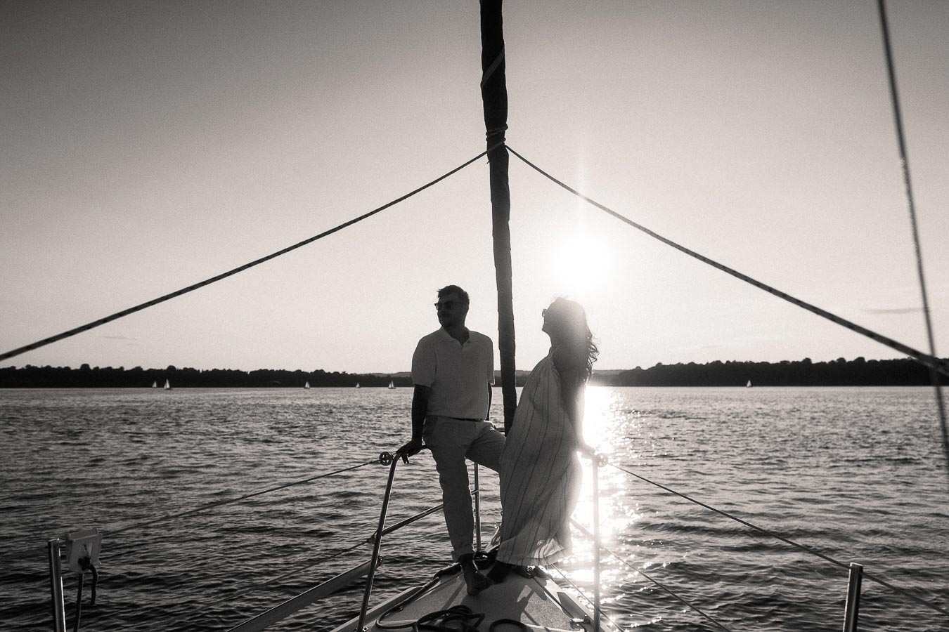 Amber and Devin silhouetted on a sailboat bow at sunset on Lake Ontario.