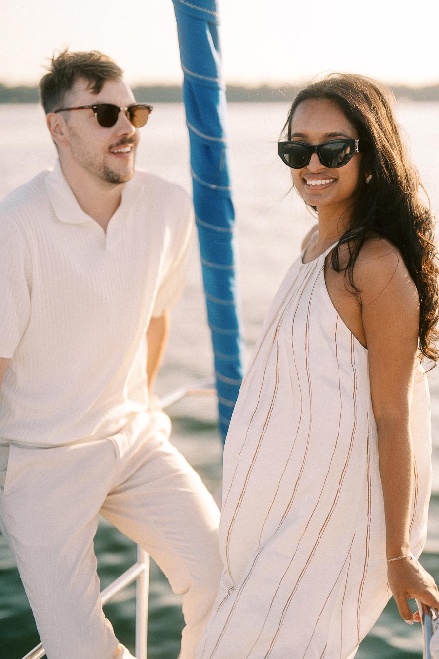Amber and Devin wearing sunglasses on a sailboat during a golden hour engagement session.