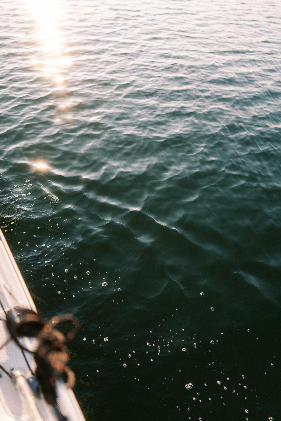 Sunlight reflecting on rippled Lake Ontario water beside a sailboat edge at golden hour.
