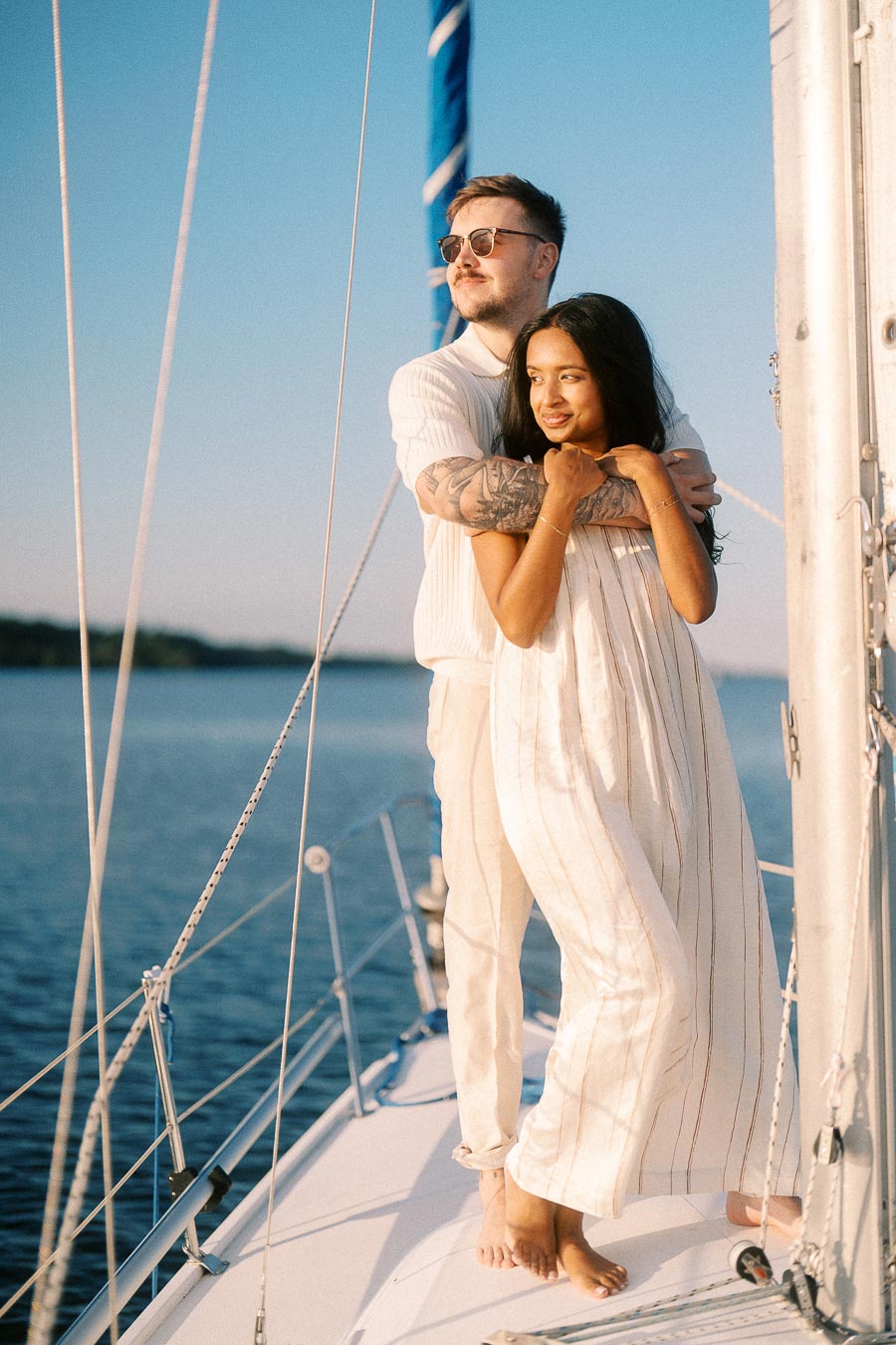 Amber and Devin embrace on a sailboat deck during a golden hour engagement session in Hamilton.