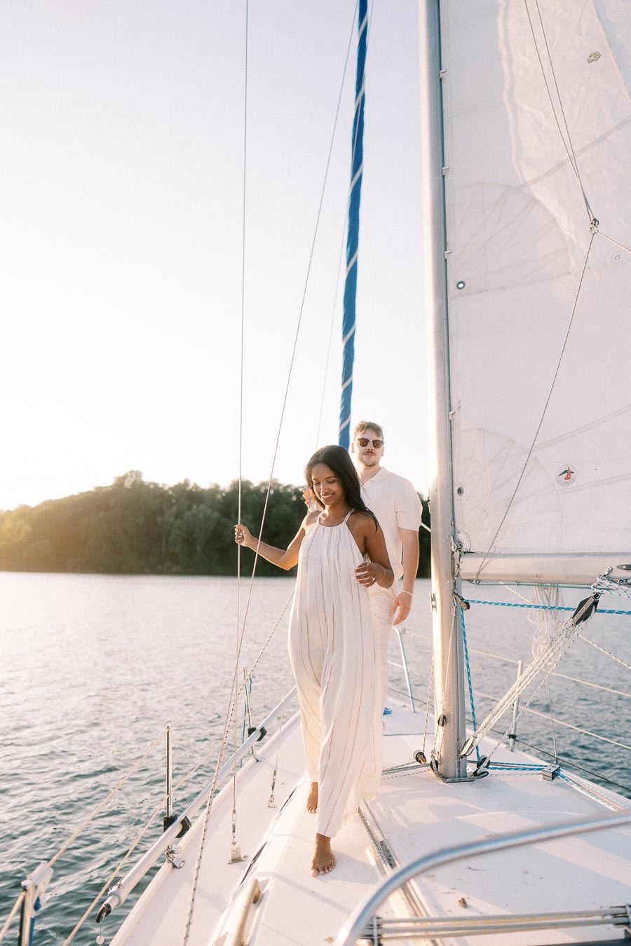 Amber and Devin walking barefoot on a sailboat deck at sunset on Lake Ontario.