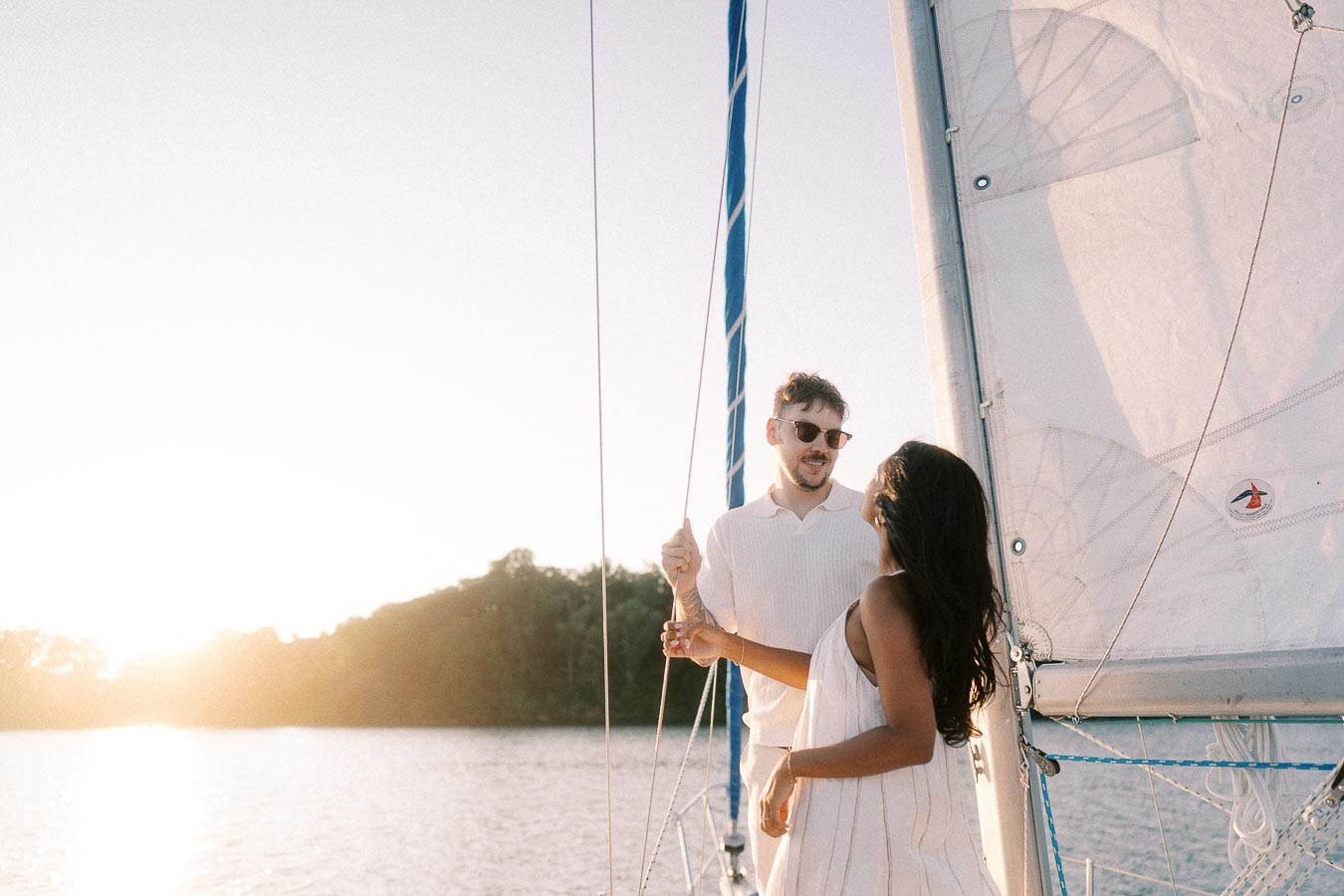 Amber and Devin standing by a sailboat mast at sunset on Lake Ontario in Hamilton.