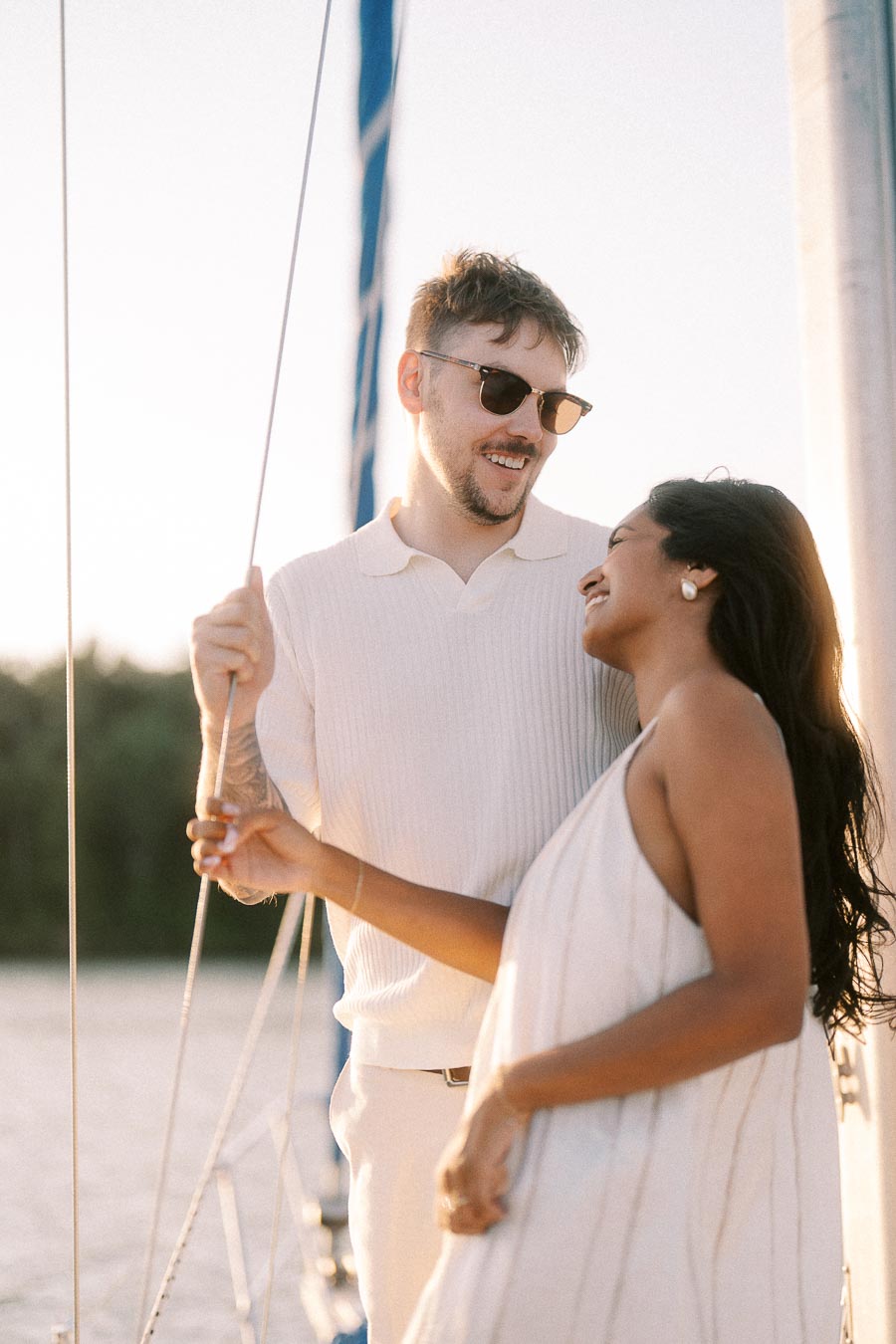 Amber and Devin smiling together on a sailboat during a golden hour engagement session.