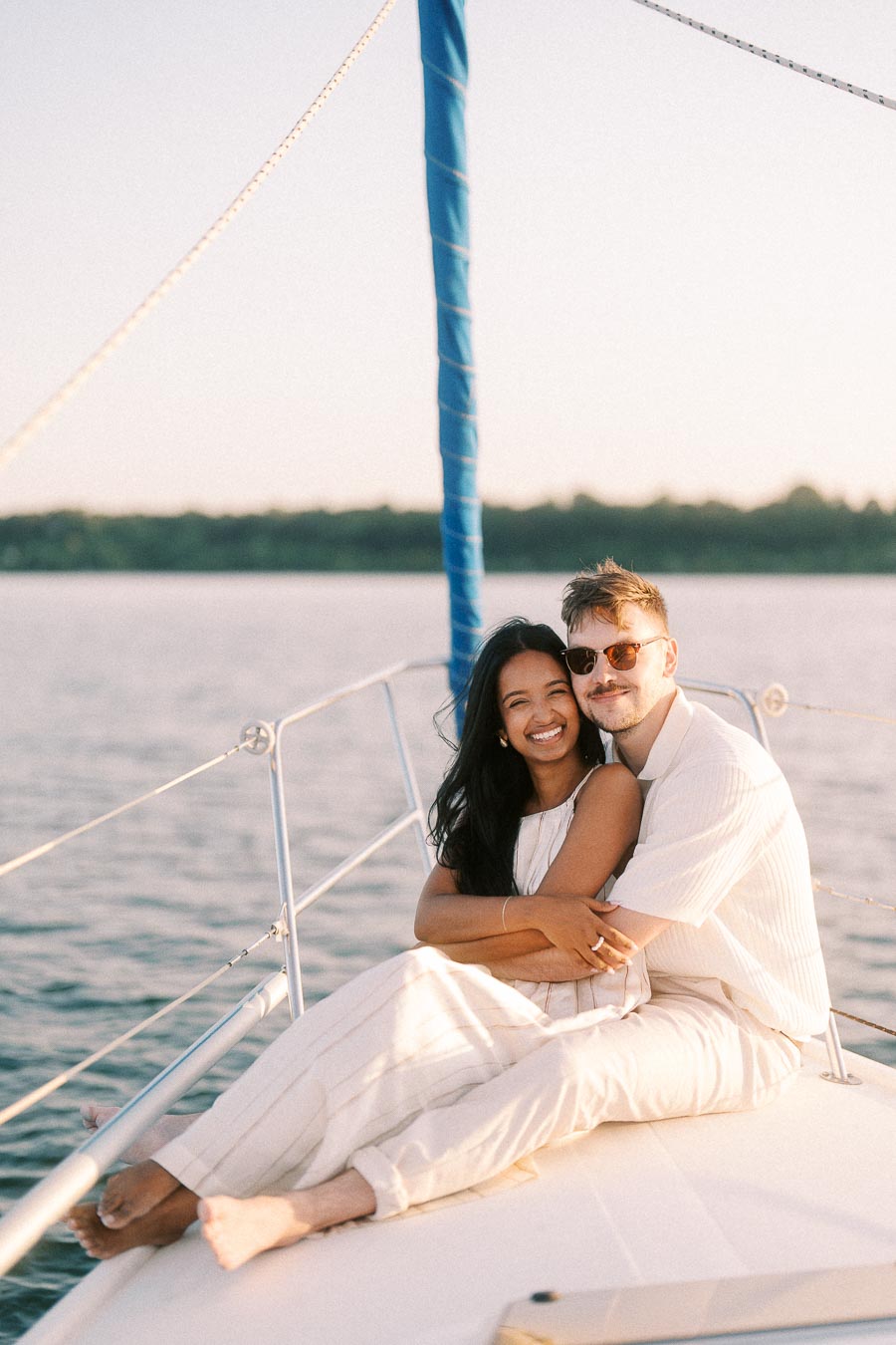 Amber and Devin cuddle on a sailboat deck at sunset on Lake Ontario.