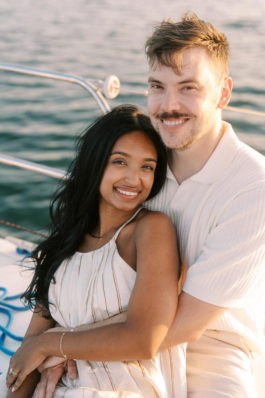 Amber and Devin smiling together on a sailboat during golden hour on Lake Ontario.