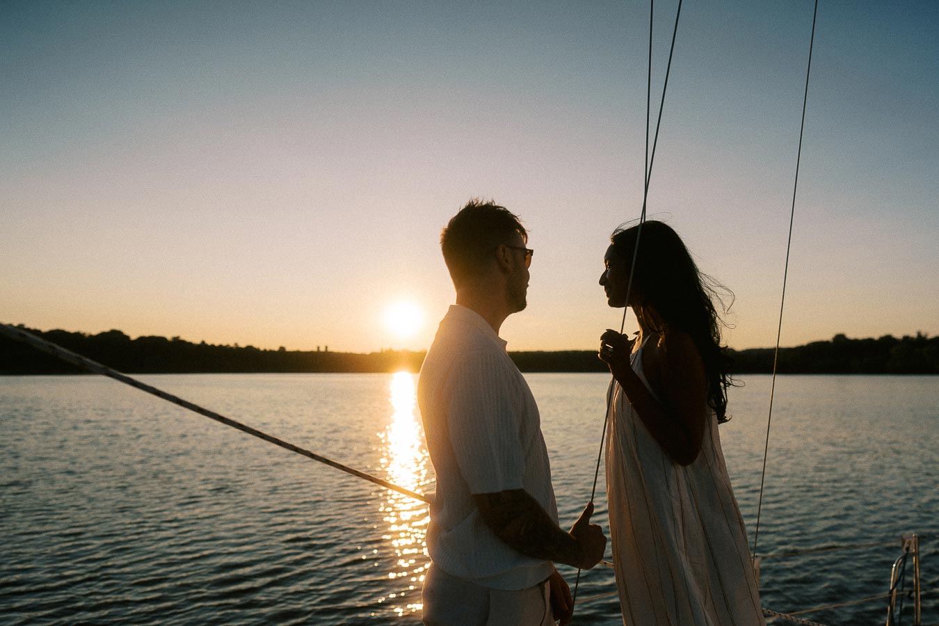 Silhouetted couple on a sailboat at sunset during a Lake Ontario engagement session.