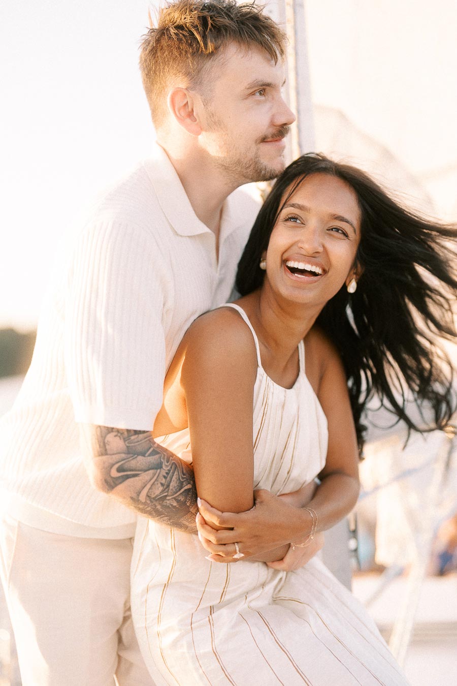 Amber and Devin laughing together on a sailboat during a golden hour engagement session.