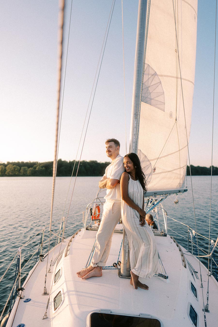 Amber and Devin standing barefoot on a sailboat deck at golden hour on Lake Ontario.