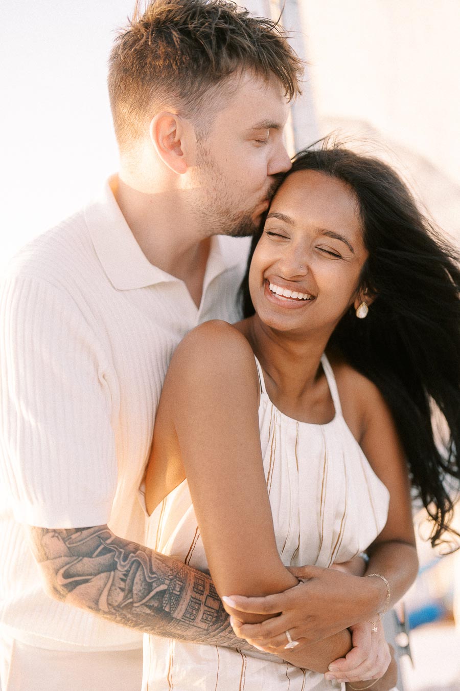 Amber and Devin embracing as he kisses her forehead during a golden hour sailboat engagement session.
