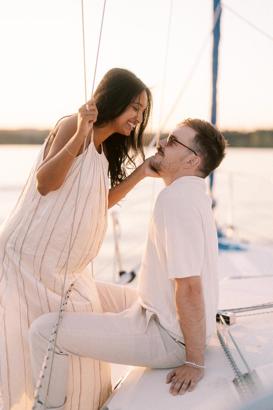 Amber and Devin smiling together on a sailboat during a golden hour engagement session.