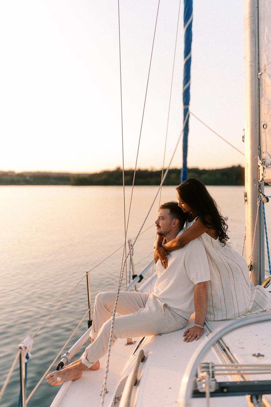 Amber and Devin sit together on a sailboat at sunset on the Hamilton waterfront.