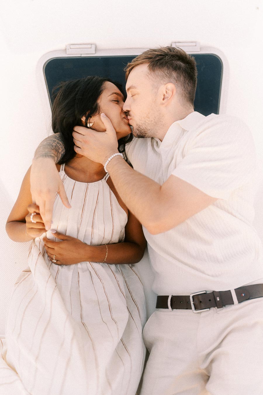 Amber and Devin kissing while lying together on a sailboat during their engagement session.