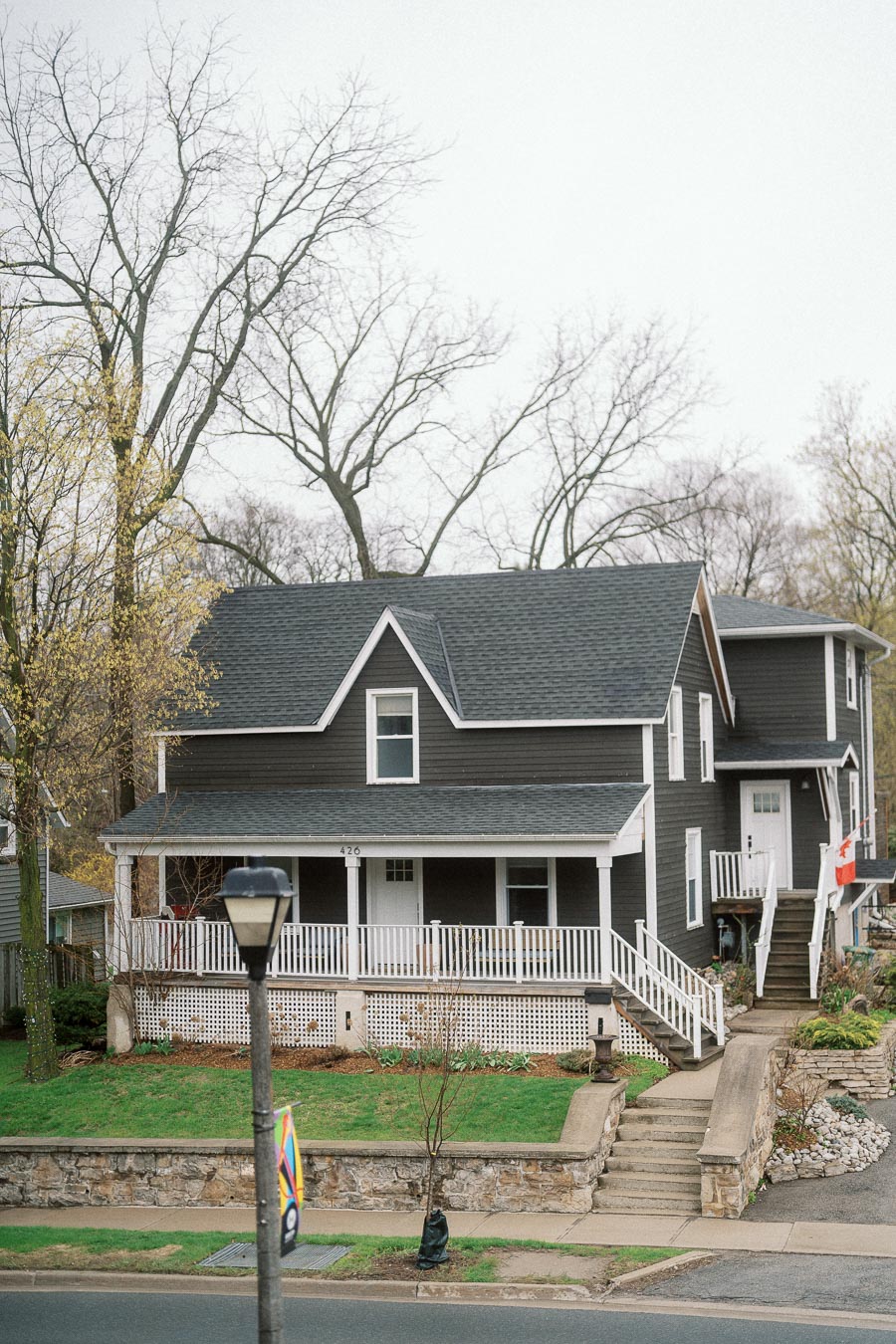 Gray two-story house with a white porch, front steps, and bare trees behind it