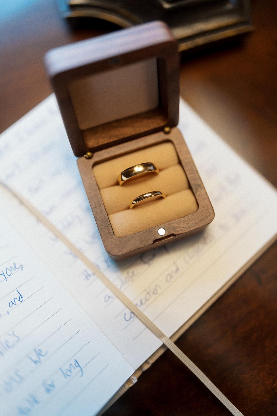 Two gold rings displayed in a wooden ring box on an open handwritten notebook.