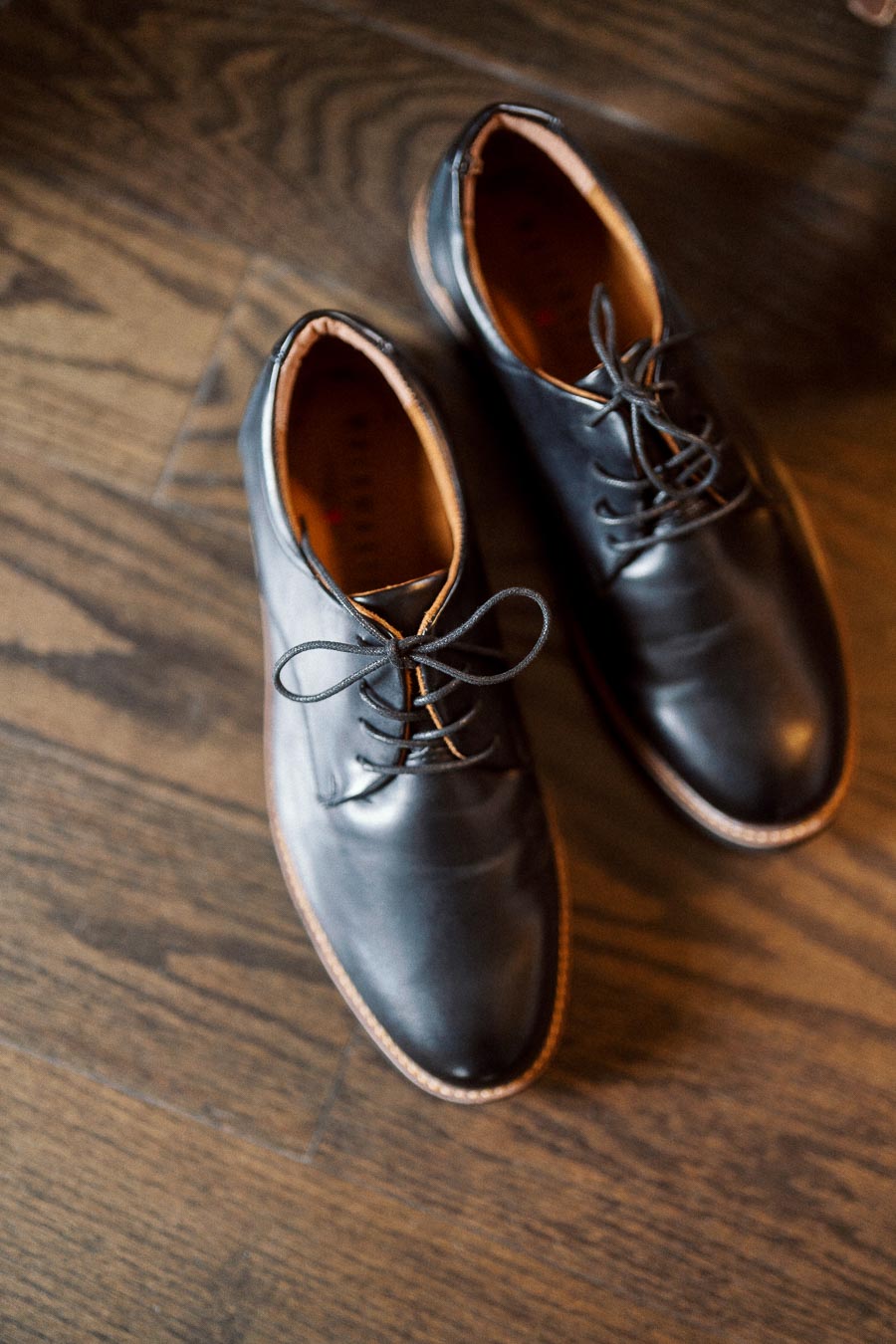 Black leather dress shoes with laces on a wooden floor