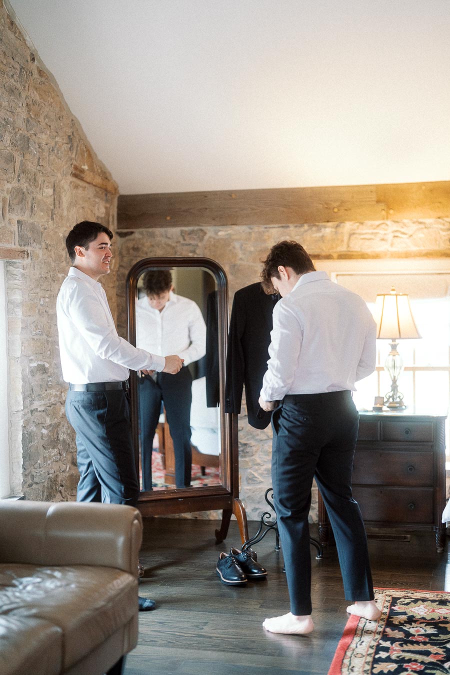 Two men getting dressed in a stone-walled room before an engagement photoshoot