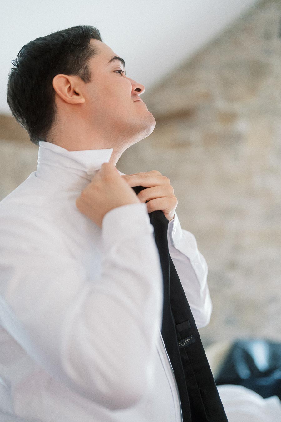 Man adjusting his black tie and white shirt collar indoors.