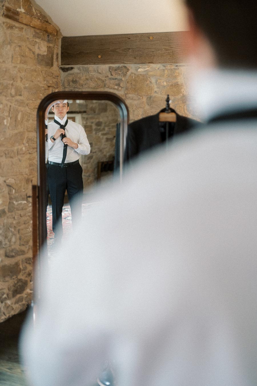 Man adjusting his tie while reflected in a full-length mirror