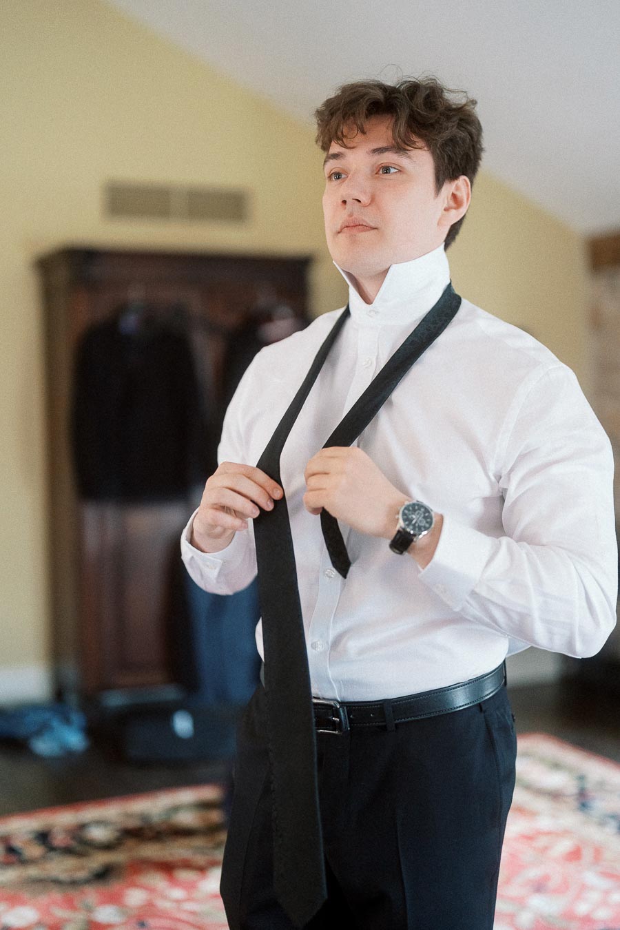 Man in a white dress shirt adjusting a black tie indoors