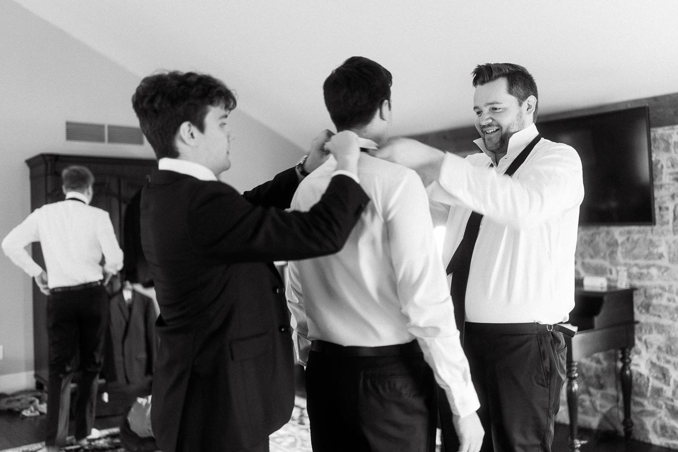Groomsmen helping a man adjust his shirt collar before a formal event