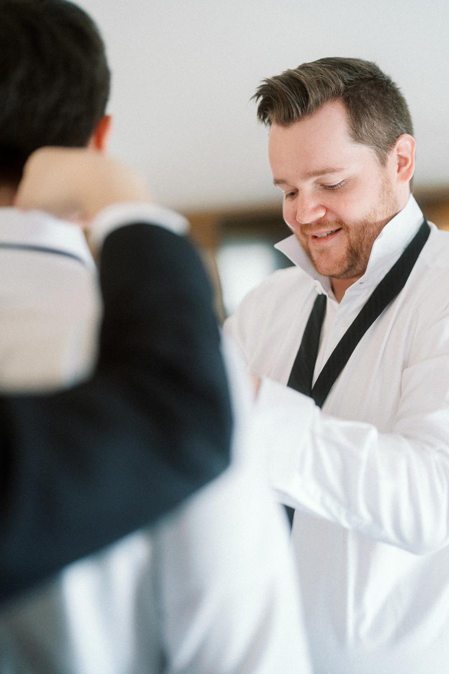 Man smiling while adjusting formalwear beside another person indoors