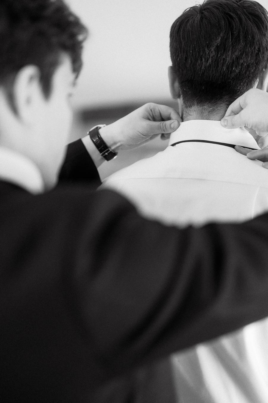 Person adjusting a man's shirt collar during a formal getting-ready moment