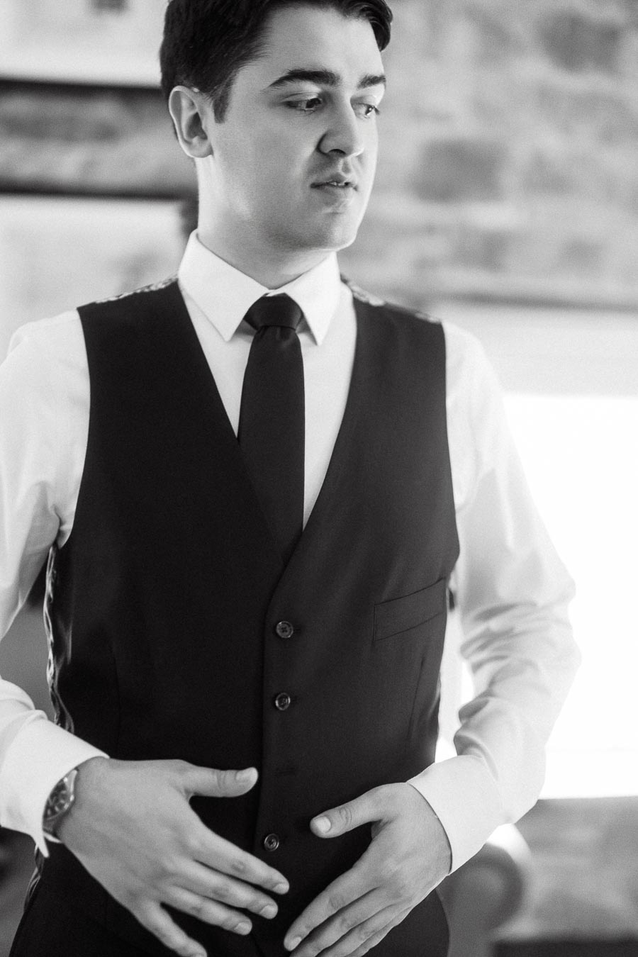 Black-and-white portrait of a man adjusting his vest and tie indoors
