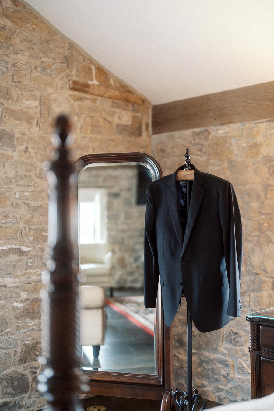 Dark suit jacket hanging in a stone-walled room beside a full-length mirror.