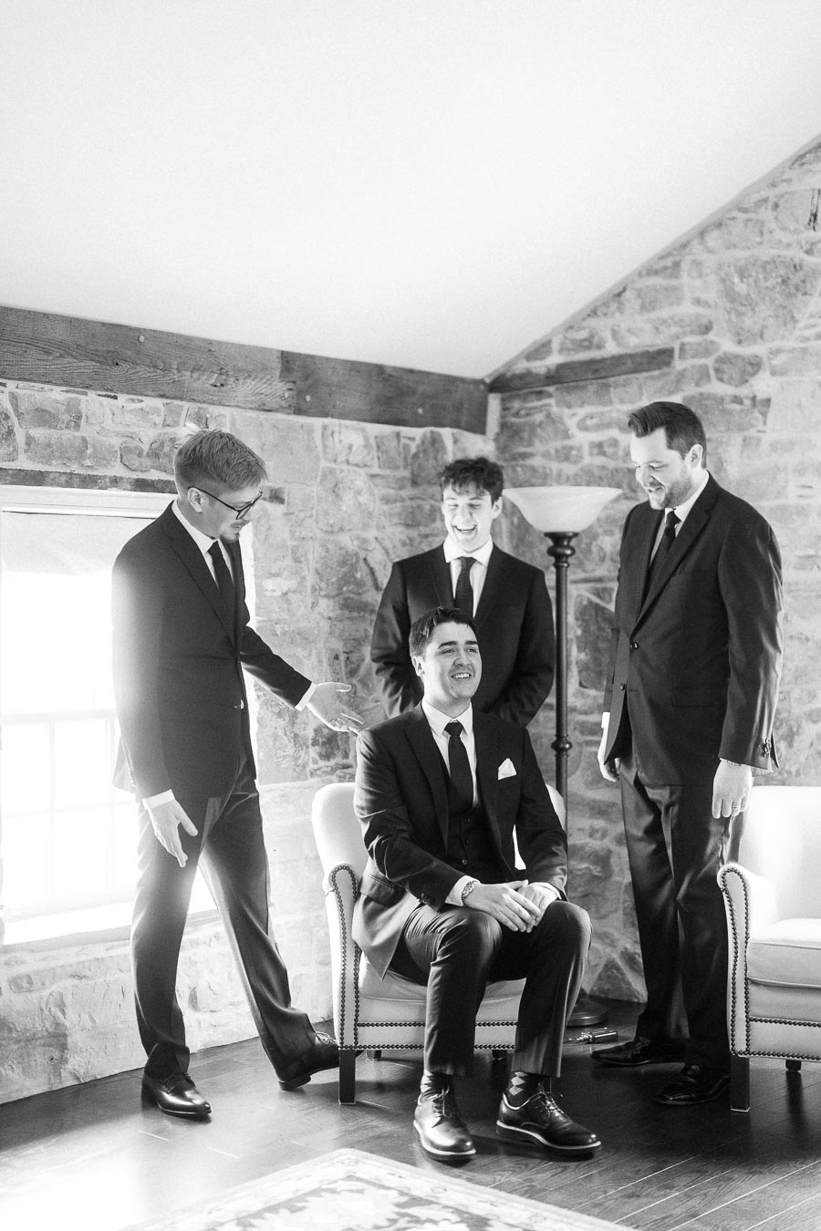 Four men in suits laughing together in a stone-walled room.