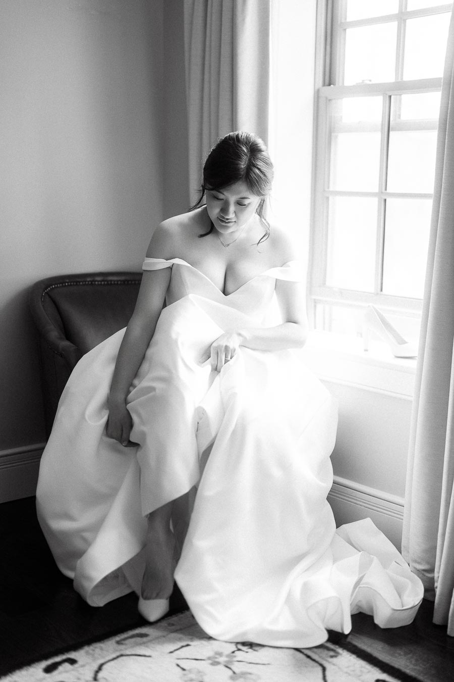 Bride in an off-the-shoulder gown seated by a bright window