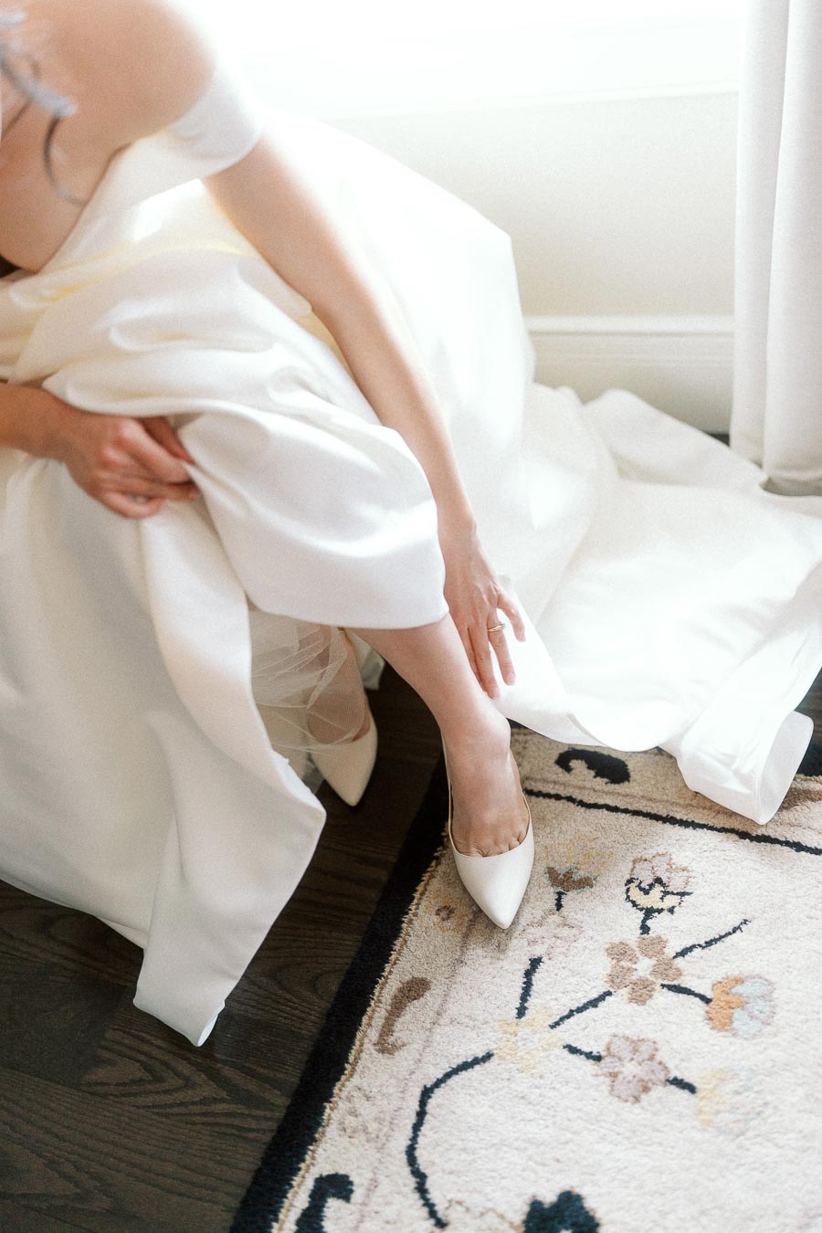 Bride adjusting a white pointed heel beneath her dress
