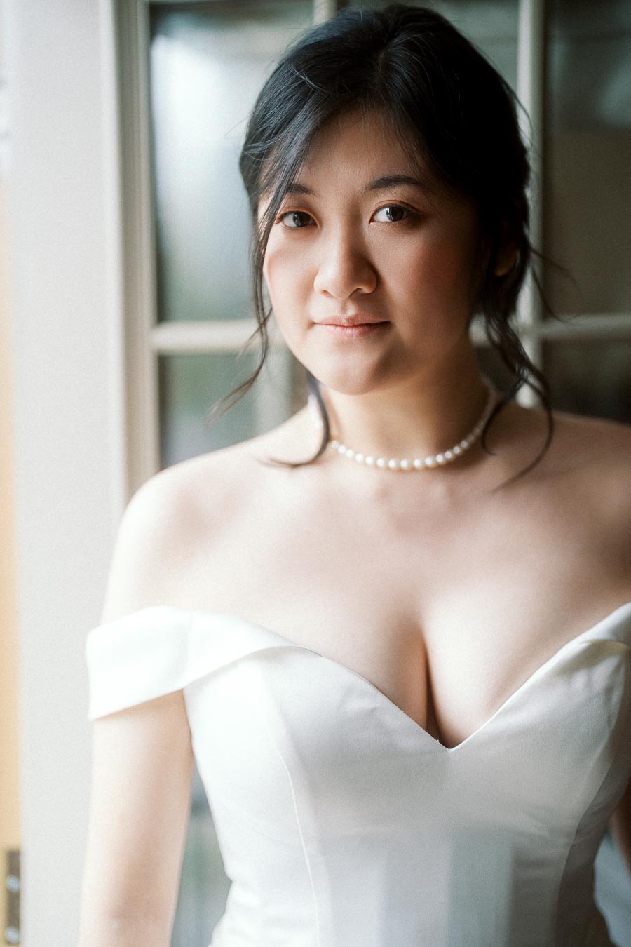 Bride-to-be in a white off-the-shoulder dress standing by a window