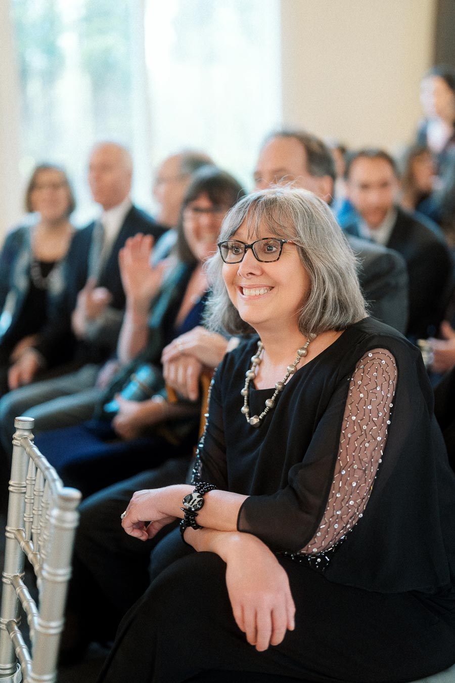 Smiling woman seated among guests at an indoor celebration