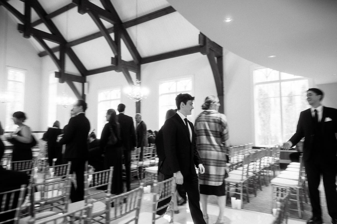 Black and white scene of guests gathering among ceremony chairs in a bright hall