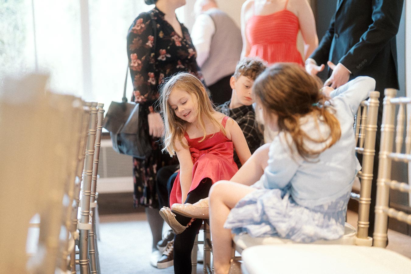 Children sitting and playing among ceremony chairs while adults stand nearby.