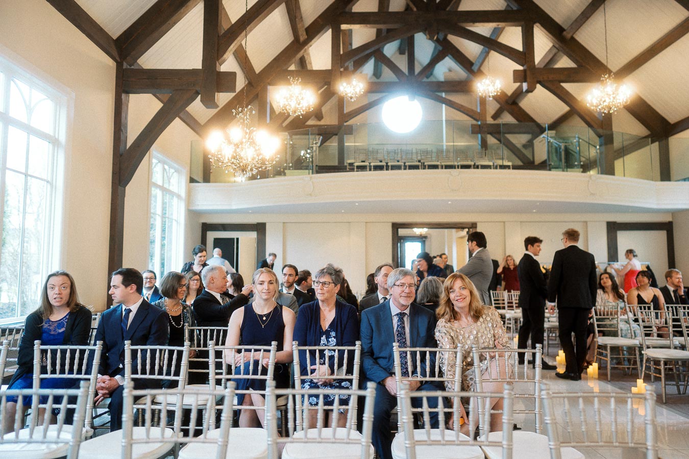 Guests seated in a bright ceremony hall with chandeliers and exposed wooden beams